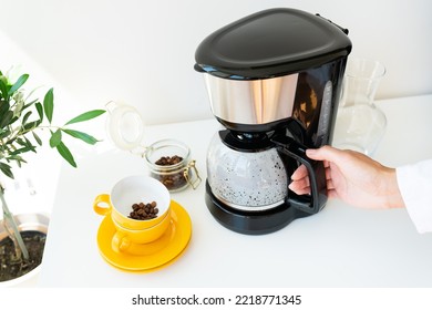 Beautiful Morning, The Girl Is Waiting For Her Coffee. Selective Focus, Noise. An Automatic Drip Coffee Maker Stands With A Yellow Cup On A White Table. Electric Kitchen Small Household Appliances