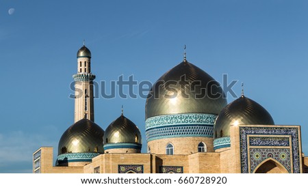 Beautiful mosque of yellow bricks, golden shine of minarets, against the background of the moon in blue sky. Summer, 2017 Kazakhstan, Kostanay.