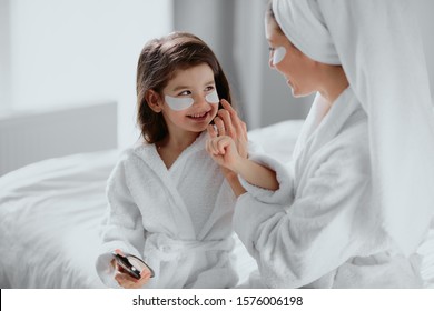 beautiful mother in bathrobe and her little daughter together with towels on head and mask on face while enjoying spa procedures isolated in white bedroom - Powered by Shutterstock