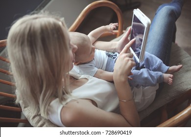 beautiful mother blonde with her baby son in her arms with a tablet in a rattan chair at home, the concept of working mom and children and gadgets, emotional lifestyle, selective focus and toning - Powered by Shutterstock