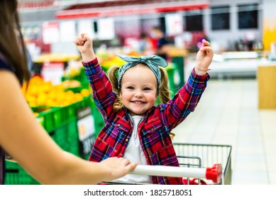 Beautiful mother carries little girl in the supermarket trolley