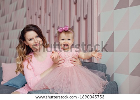 A beautiful mother with curly hair, in a pink dress, holding her daughter in a smart pink dress. Mother's day