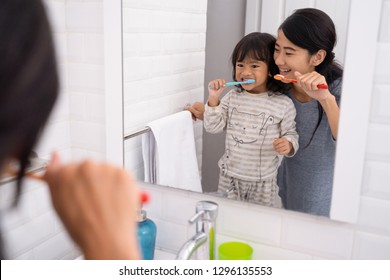 beautiful mother and daughter brushing teeth in the bathroom sink before going to bed - Powered by Shutterstock