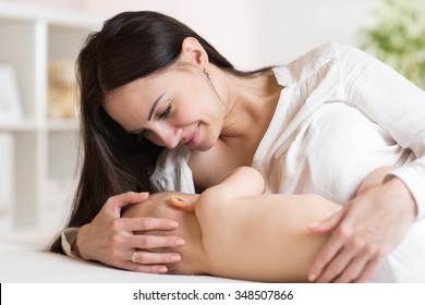 Beautiful mother feeding breast her baby in bed at home