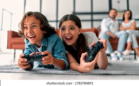 Schöne Mutter und gut aussehender Vater mit ihrer Tochter und Sohn verbringen Zeit zusammen zu Hause. Kinder spielen Videospiele. Fröhliches Familienkonzept.