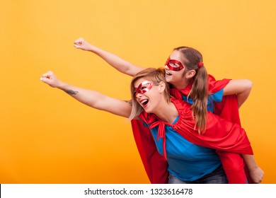 Beautiful mother and her cute little girl playing together dressed like superheros over yellow background. Good parenting. Happy kid. Mother and daughter bonding. - Powered by Shutterstock