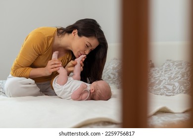 Beautiful mother kissing feet baby on bed at home - Powered by Shutterstock