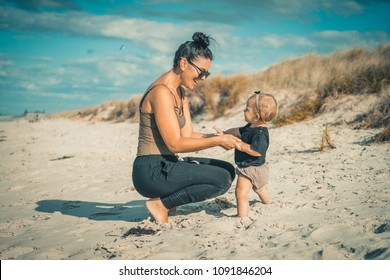 Beautiful mother playing with daughter on sunny sandy beach.