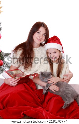 Beautiful mother and pretty daughter holding lovely gray British cat over Christmas tree on Holiday theme/Lovely mother and daughter playing with domestic animal on holiday theme