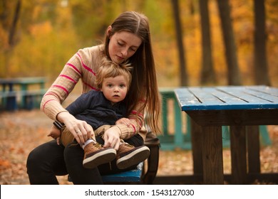 Beautiful mother tying  shoes for baby. Autumn park. Mom and son. Lifestyle. - Powered by Shutterstock