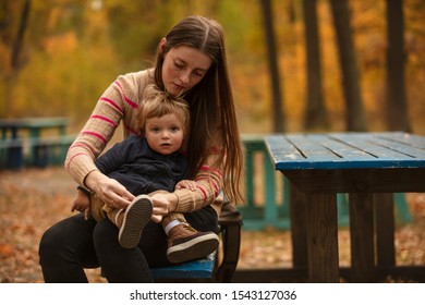 Beautiful mother tying  shoes for baby. Autumn park. Mom and son. Lifestyle. - Powered by Shutterstock