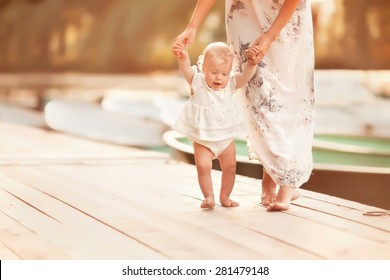 beautiful mother is walking on the pier with her little baby girl daughter with first steps - Powered by Shutterstock