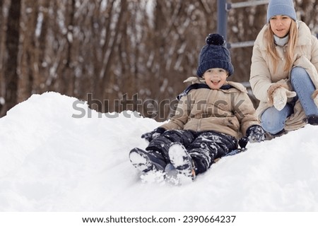 Beautiful mother in a warm jacket. Mom with little son sledding in the park. Family sledding in a winter park. Little boy in a cute hat