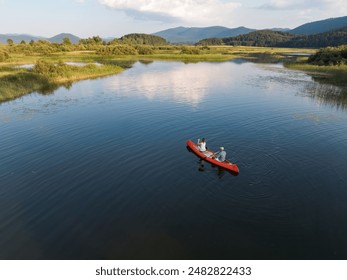 Beautiful mountain lake scenery with two people enjoying recreation paddling a red canoe, aerial shot. Summer vacation concept. - Powered by Shutterstock