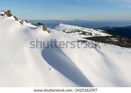 Beautiful mountain landscape. View from the snowy mountainside to the sea coast. There is white snow in the foreground. The Sea of Okhotsk is in the distance. Cold weather. Magadan region, Russia.