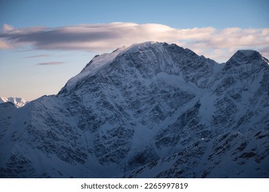 Beautiful mountain peaks in the snow in winter at sunset. Colorful landscape with high snowy cliffs in fog, blue sky with clouds on a cold evening