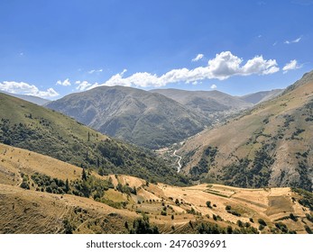 A beautiful mountainous landscape under a clear blue sky, with rolling hills and a valley dotted with patches of greenery and pathways. - Powered by Shutterstock