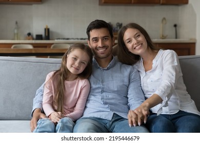 Beautiful Multi Ethnic Family Portrait, Bank Loan, Tenancy Concept. Preschool Daughter, Her Young Lovely Mother And Handsome Hispanic Stepfather Smile Staring At Camera Posing Seated On Sofa At Home