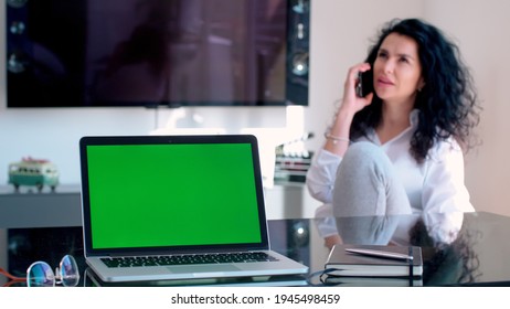 Beautiful Multi Ethnic Young Business Woman On The Phone In Home Office Wear Cozy Jogging Pants With Green Screen On Laptop In Foreground