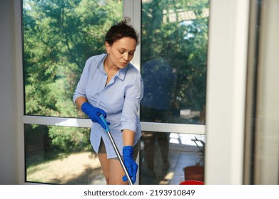 Beautiful Multi-ethnic Young Woman, Homemaker, Maid In Blue Rubber Gloves, A Lovely Housewife Wiping The Floor In A Veranda With Mop. Housekeeping. Domestic Chores. Housework. Cleaning Service.