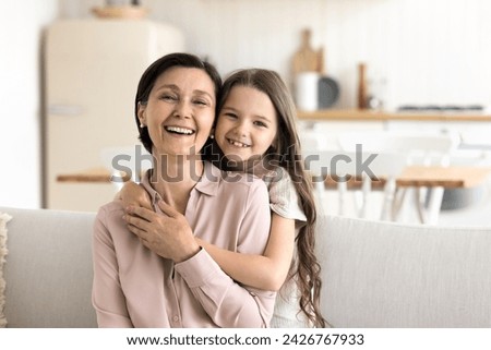 Beautiful multigenerational family ties, bond, harmonic relationships. Cute little 5s granddaughter and pretty mature granny hugging, laughing, looking at camera, feel love, showing support and care