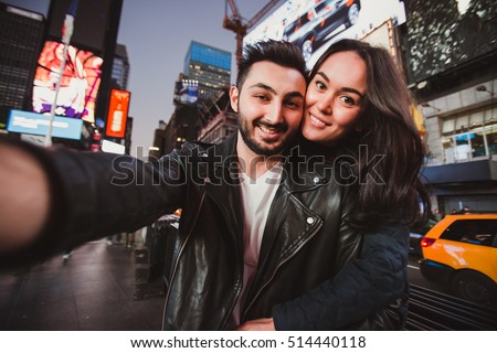 Beautiful multiracial couple in love taking selfie photo for blog on Times Square in New York while travel across USA