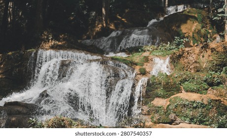Beautiful multi-tier waterfall cascading through a lush tropical rainforest, featuring mossy rocks, flowing freshwater, dense forest, eco tourism, peaceful wilderness, and scenic natural landscape.