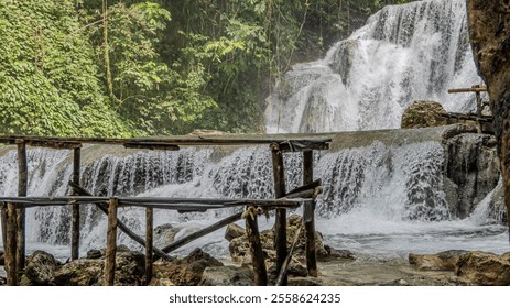 beautiful multi-tiered waterfall flows through lush greenery and wooden structures. - Powered by Shutterstock