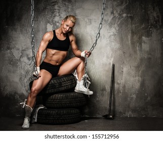 Beautiful muscular bodybuilder woman sitting on tyres and holding chains  - Powered by Shutterstock