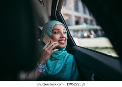 Beautiful Muslim Arabian Woman With Hijab Sitting On Backseat In Luxury Car. She Using Her Smart Phone And Looking Through Window.