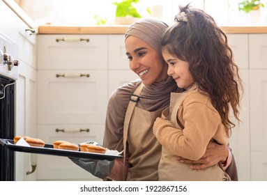 Beautiful Muslim Mom In Hijab And Her Cute Little Daughter Baking Together In Kitchen, Smiling Islamic Mother And Kid Putting Tray With Fresh Baked Muffins Out Of Oven, Closeup Shot With Free Space