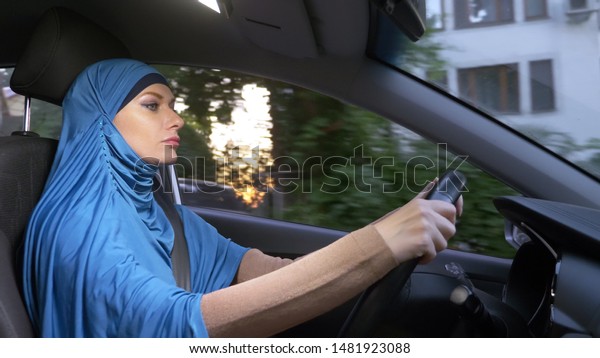 beautiful muslim woman in blue\
hijab driving a car. rides during the day on the streets of the\
city.