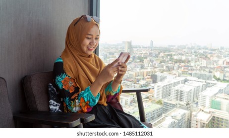 Beautiful Muslim woman in headscarf and fashionable modern trendy clothes use smartphone and sitting againts cityscape on day time - Powered by Shutterstock