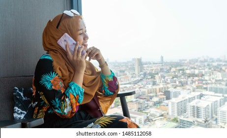 Beautiful Muslim woman in headscarf and fashionable modern trendy clothes takes phone call and sitting while looking at cityscape on day time - Powered by Shutterstock