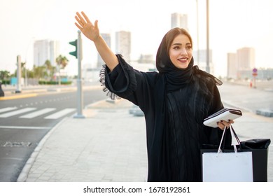 Beautiful muslim woman with shopping bags, phone and wallet hitching a taxi on the street - Powered by Shutterstock