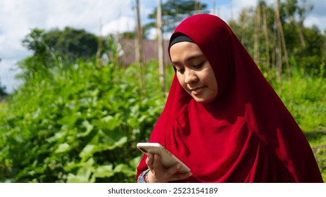 beautiful muslim woman smiling wearing red hijab in park while holding smartphone - Powered by Shutterstock