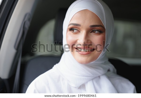 Beautiful muslim woman in white hijab sitting on the\
back seat of a luxury\
car