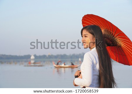 A beautiful Myanmar woman with traditional dress and holding red umbrella standing near the lake ,U-beng bridge,Mandalay Myanmar.