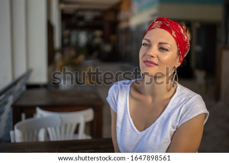 Beautiful mysteriously smiling blonde in white clothes, a red bandana, in a beach bar, near a high table