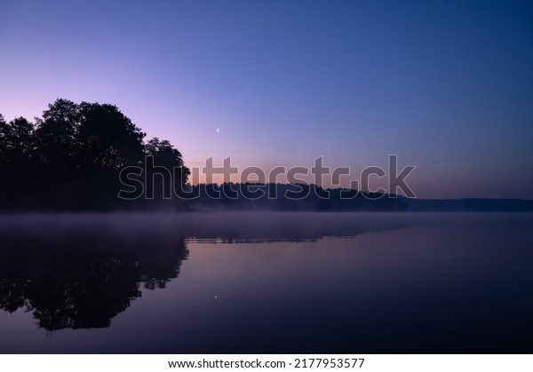 Beautiful mystical\
landscape. Forest lake at summer night before sunrise. Fog above\
calm water. Scenic\
nature.