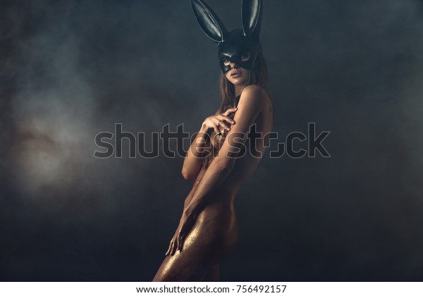 Beautiful naked woman in fashion bunny mask. Body\
covered with gold\
glitter