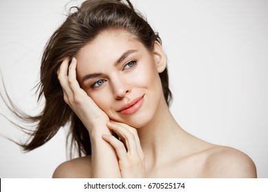 Beautiful naked young girl with perfect clean skin smiling touching hair over white wall. Facial treatment.