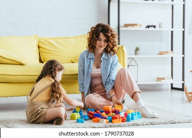 Beautiful Nanny And Child Sitting On Floor In Living Room And Playing With Building Blocks