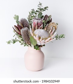 Beautiful native flower arrangement in a stylish pink vase. In the flower bunch is Eucalyptus leaves, Pink King Proteas plus purple and yellow Banksias, photographed on a white background. - Shutterstock ID 1984102949