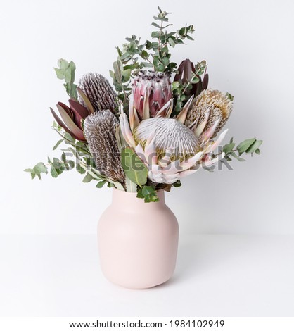 Beautiful native flower arrangement in a stylish pink vase. In the flower bunch is Eucalyptus leaves, Pink King Proteas plus purple and yellow Banksias, photographed on a white background.