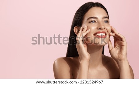 Beautiful natural girl smiling, rubbing her face with facial cleanser for glowing healthy skin, looking happy. Curly young woman showering, using skincare hydrating products, pink background.