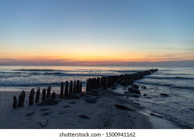 beautiful natural scene, old breakwaters in the sea at dusk against the background of an orange sunset