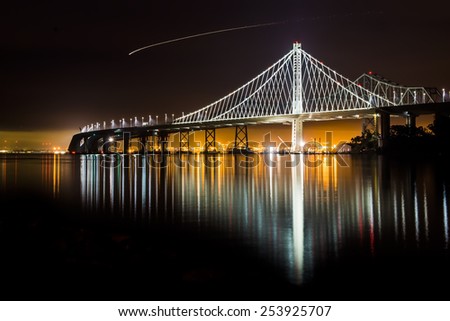 Beautiful new East Span Bay Bridge at night illuminated reflecting Oakland port color lights cityscape. The iconic and majestic bridge after dark long exposure in San Francisco greets traveler.