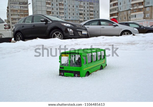 Beautiful new green bus busted in fresh white\
snow. Bus model in the snow against the backdrop of large cars and\
Soviet high-rises