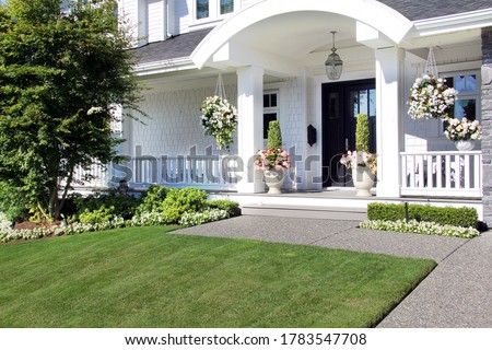 Beautiful new luxury home exterior in summer. Custom house with a porch and professional landscaping in Canada. 